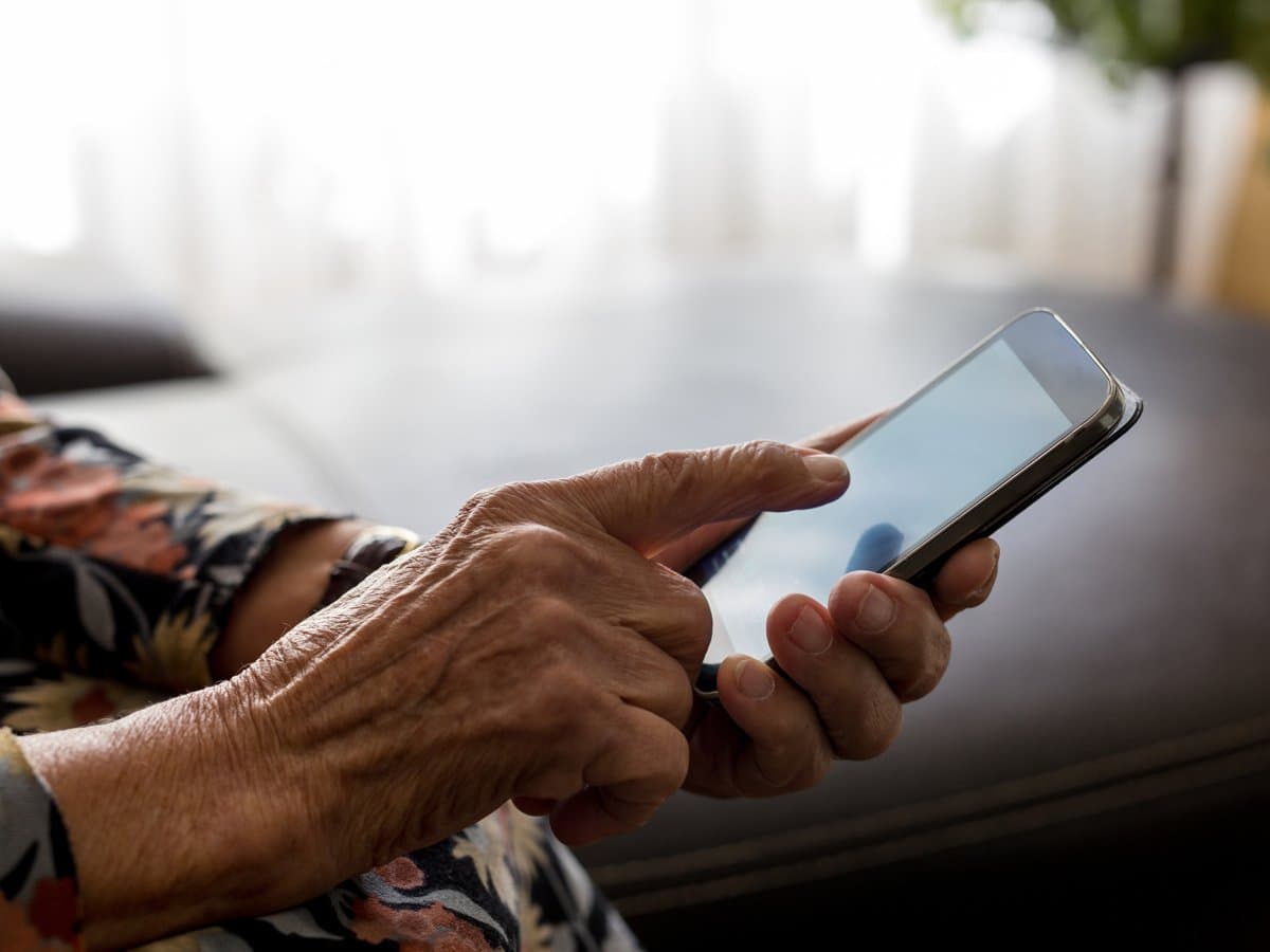 Händer på en äldre person som håller i en mobiltelefon