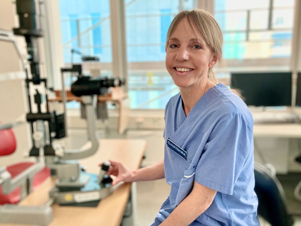 En kvinna i sjukhuskläder sitter bredvid ett mikroskop.