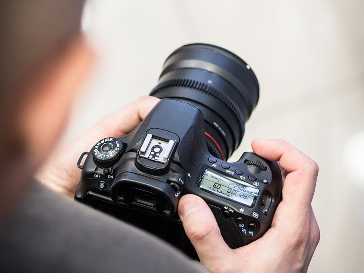 En kamera som en person håller. Personen som håller kameran i förgrunden syns suddigt.