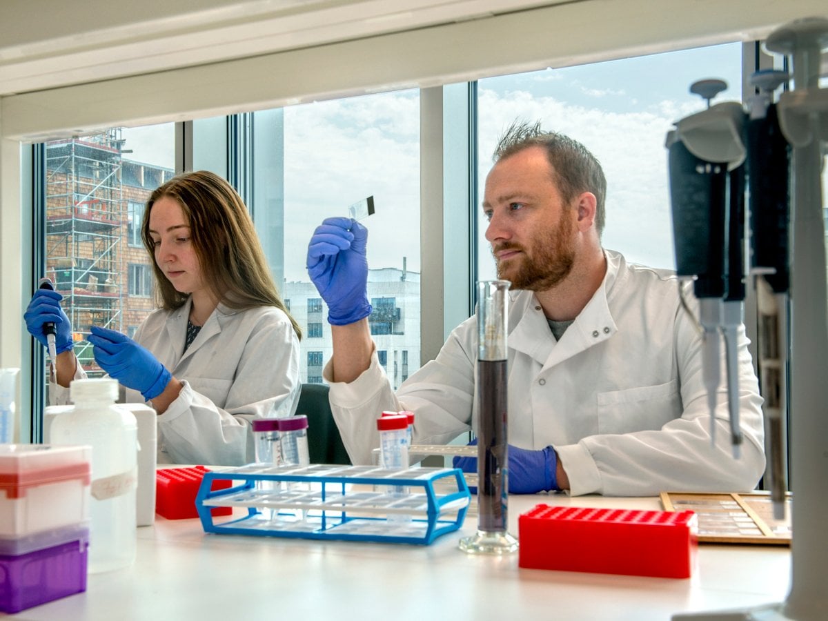 Två forskare i vit labbrock och blåa handskar.