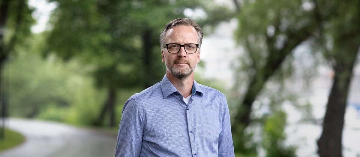 En man i blå skjorta och glasögon står på en gata.