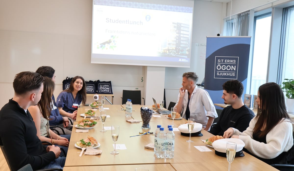 En grupp människor som sitter runt ett konferensbord. Studentmössor ligger på bordet