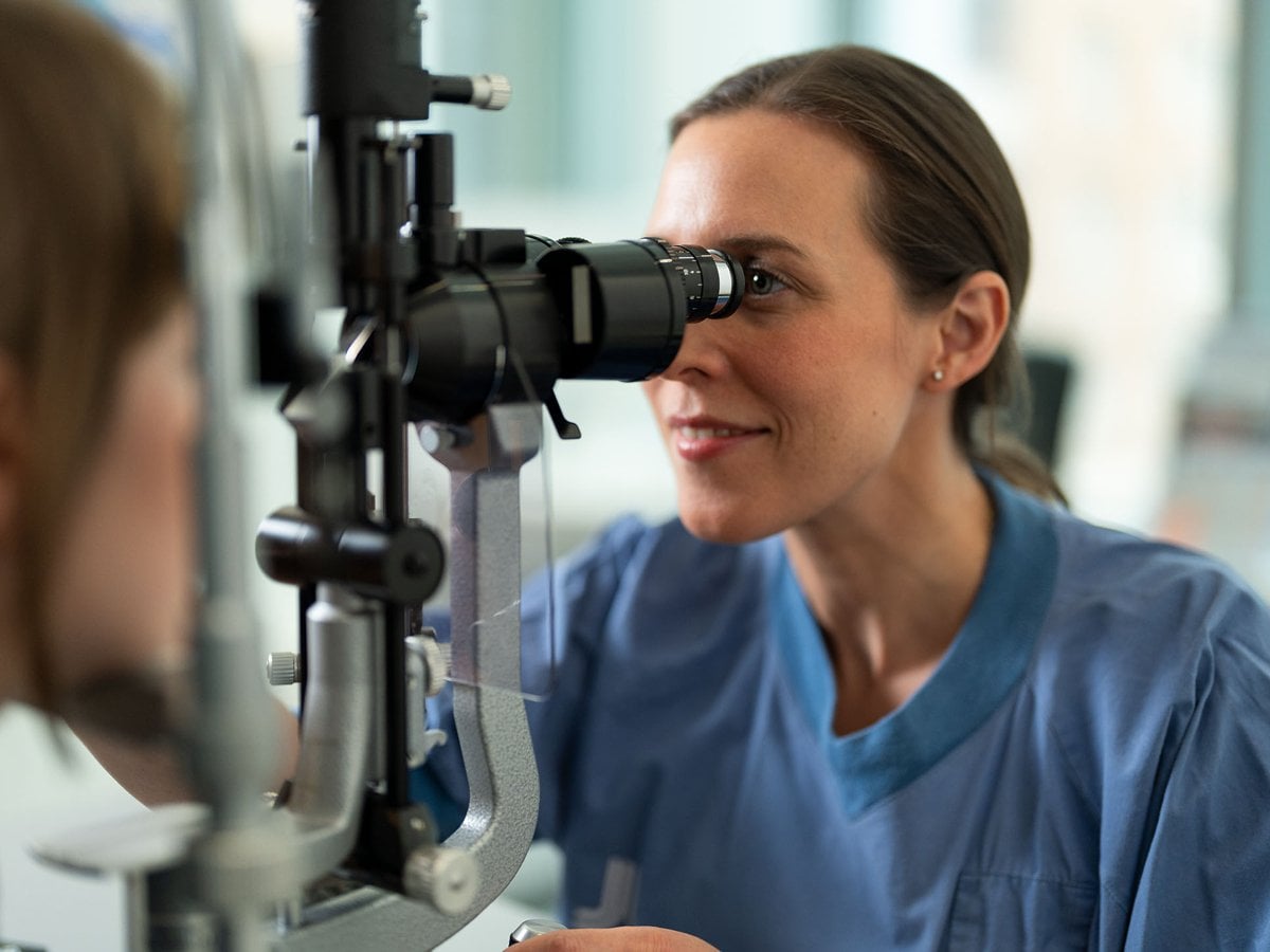 En kvinnlig läkare i blå sjukhuskläder undersöker ögat på en patient.