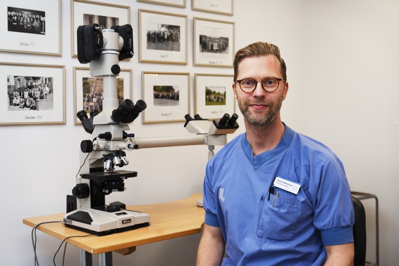 En man i blå skjorta står framför ett mikroskop.