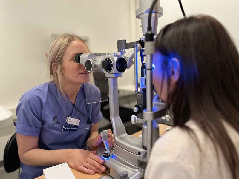 En sjuksköterska i vårdkläder som genomför en ögonundersökning i ett mikroskop.
