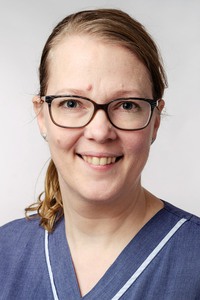 En kvinna i glasögon och uppsatt hår med sjukhuskläder.