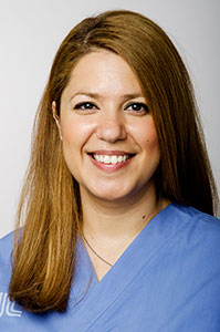 En mörkblond kvinna med blå sjukhusuniform som ler.