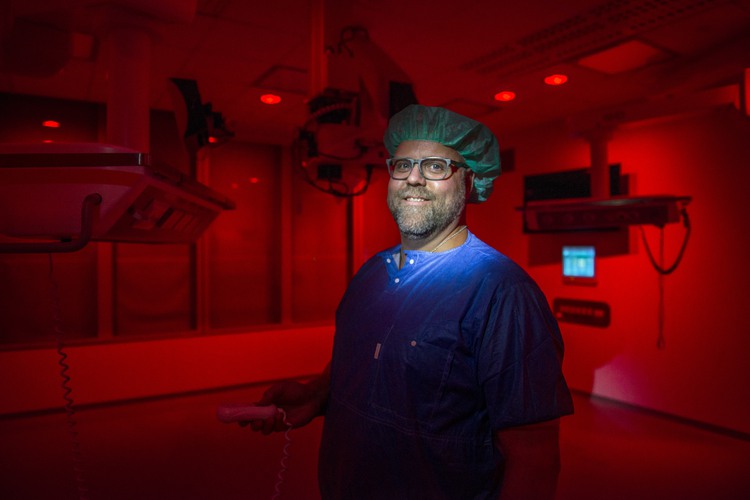 En man i operationskläder som står i en operationssal med rött ljus.
