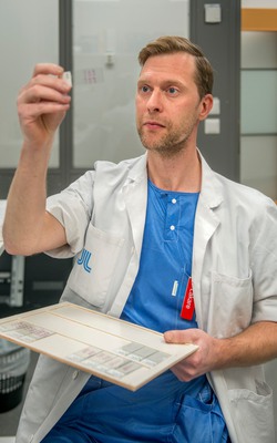 En man i sjukhusuniform studerar ett prov på en glasplatta.
